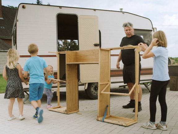 Adulte et deux enfants travaillant sur le cadre en bois d'une caravane.