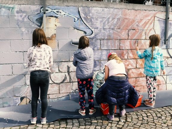 Des enfants peignent en blanc un vieux mur.